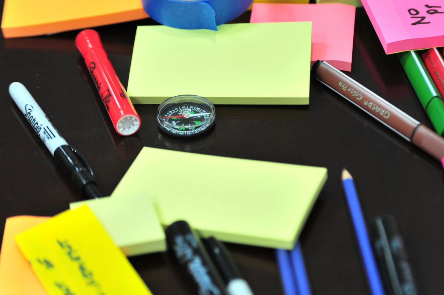 A compass, Post It notes, flip chart markers, sharpies laid on a black table.